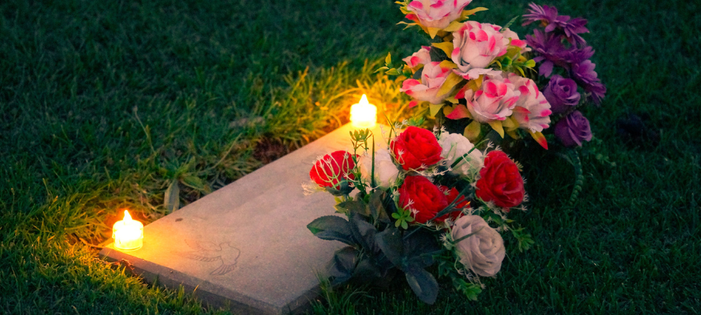 Rosas rojas, rosadas, moradas y blancas en una lapida con velas en la noche