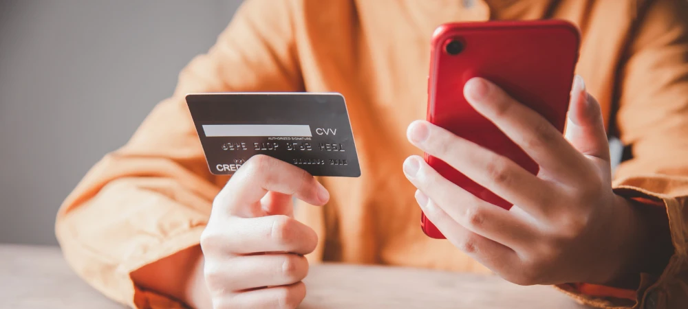 Persona pagando online con tarjeta de crédito y un smartphone rojo