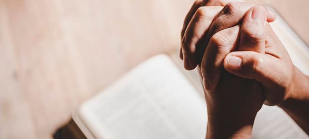 Manos orando sobre biblia